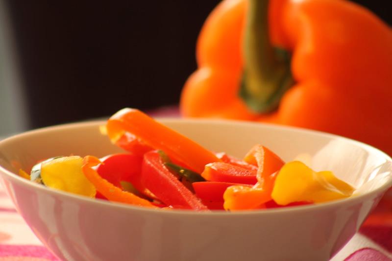 White bowl with slices bell peppers and bell pepper out of focus in background.