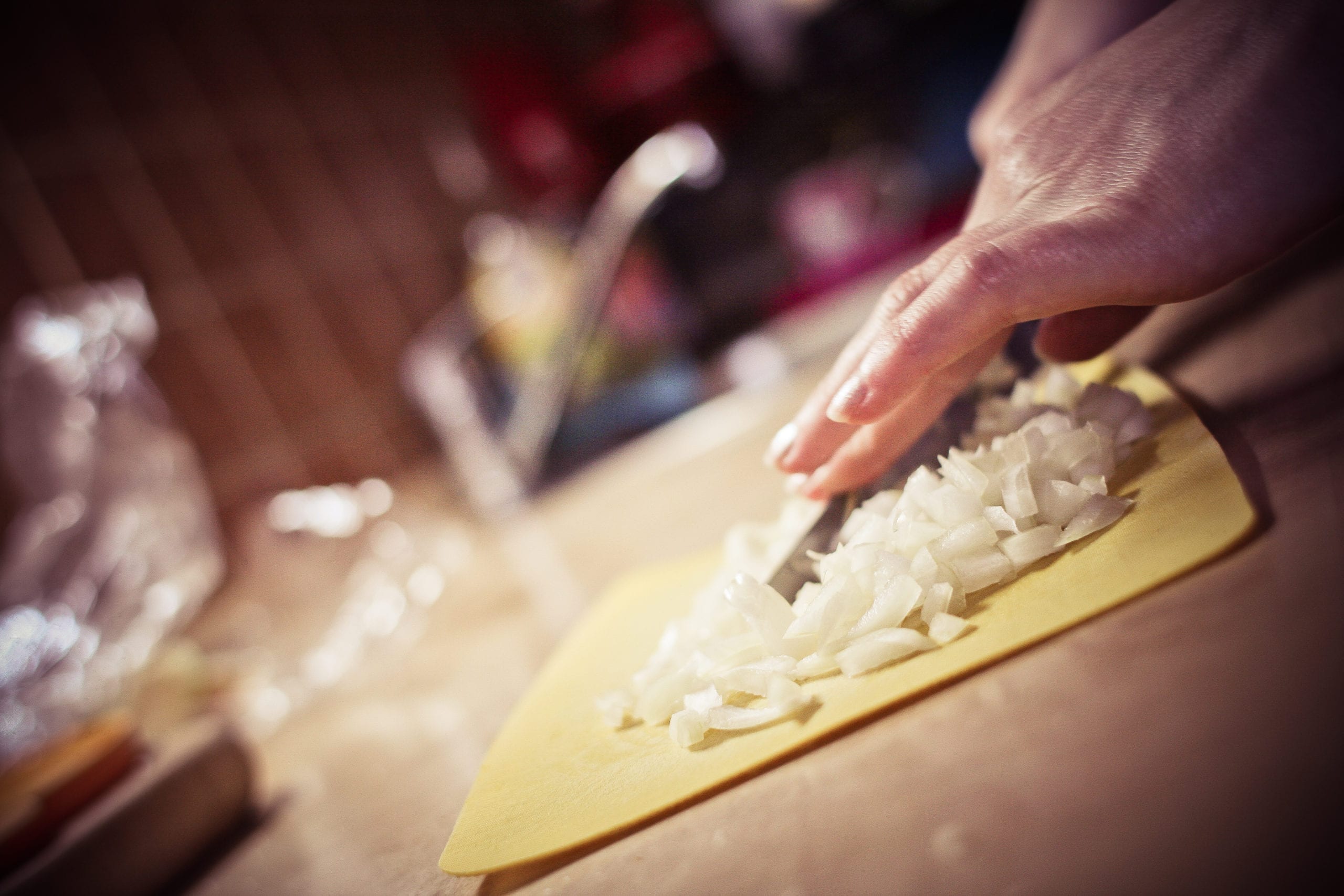 Yellow cutting board on a counter with diced onions