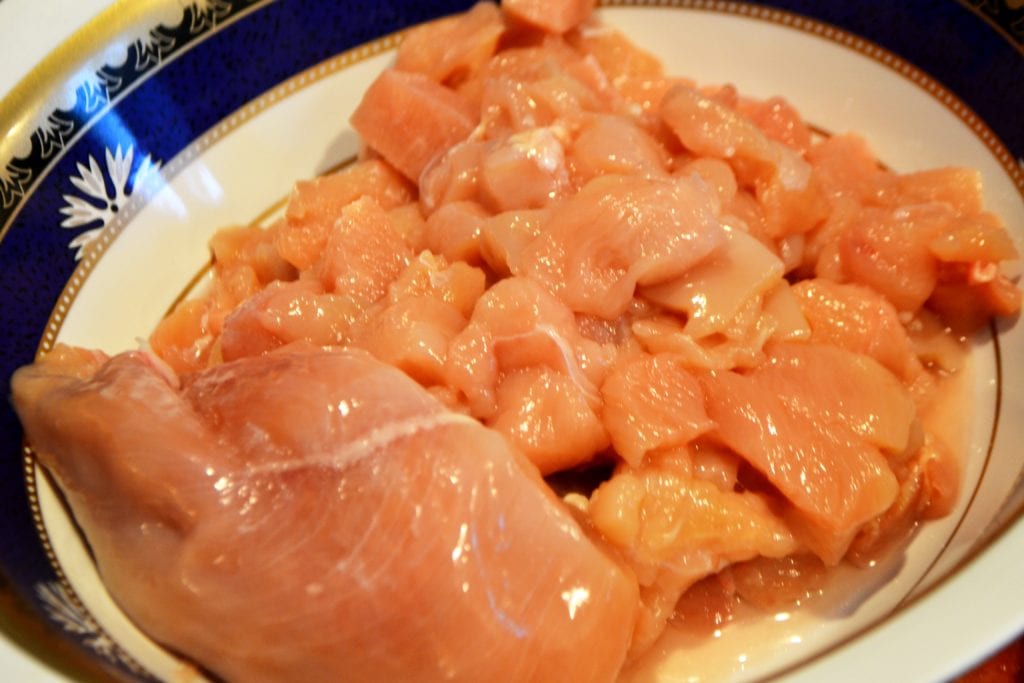 Diced chicken breast in a bowl with one half whole chicken breast.