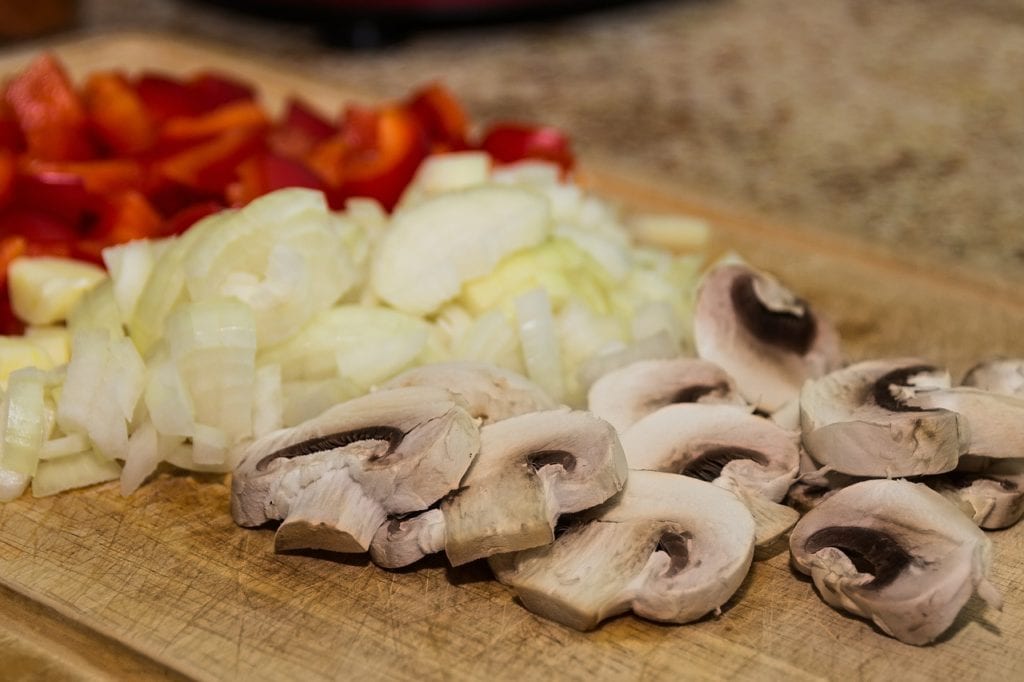 Cutting board with sliced onions, mushrooms, and red peppers