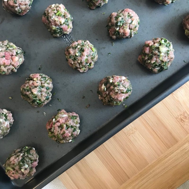 Baking tray with kafta meatballs sitting on a cutting board.